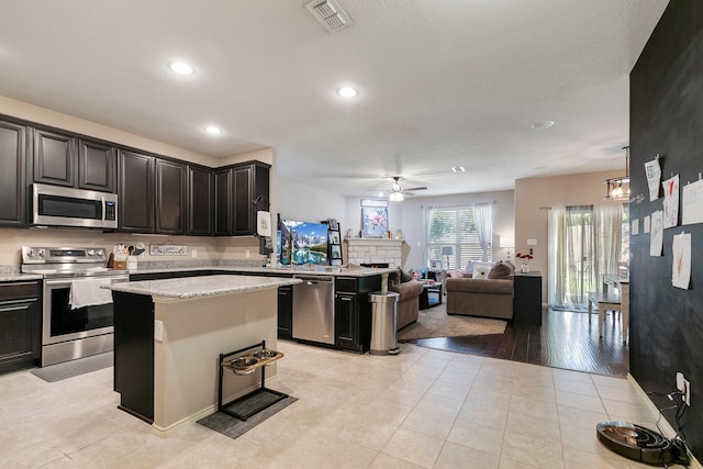 kitchen featuring light tile patterned floors, stainless steel appliances, a fireplace, a kitchen island, and decorative light fixtures