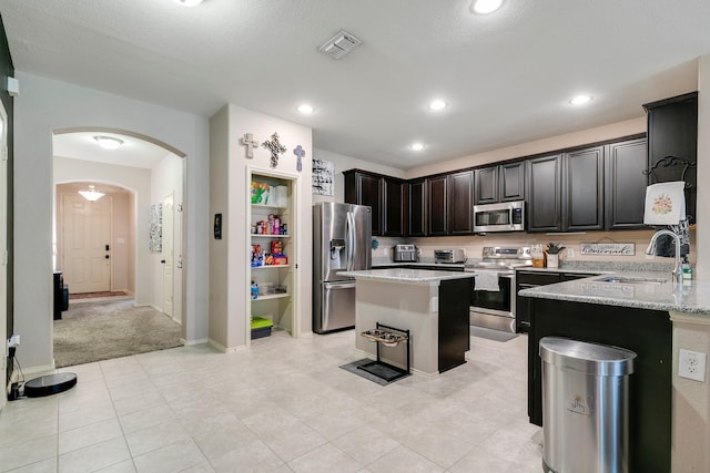 kitchen with sink, light colored carpet, kitchen peninsula, stainless steel appliances, and light stone countertops