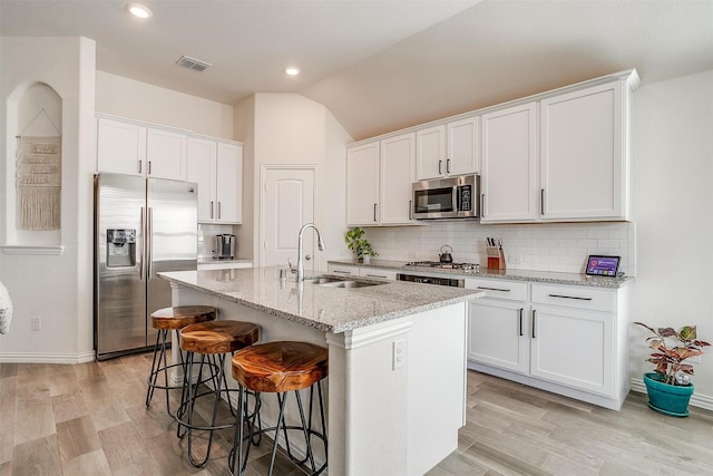 kitchen with white cabinetry, sink, a kitchen island with sink, stainless steel appliances, and light stone countertops