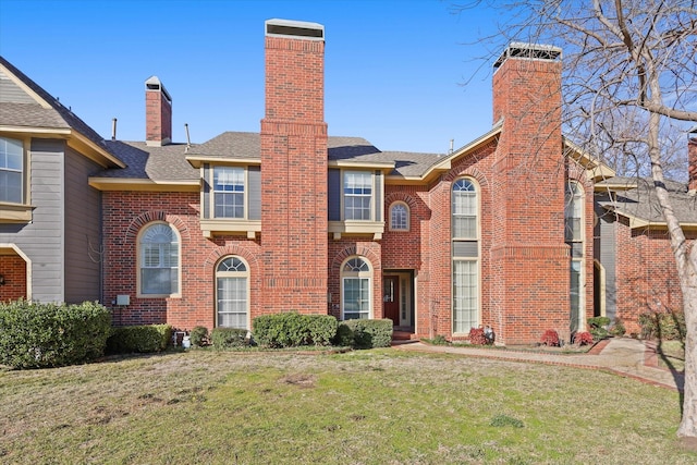 view of front of home featuring a shingled roof, a chimney, a front lawn, and brick siding