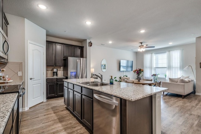 kitchen with sink, dark brown cabinets, a center island with sink, light hardwood / wood-style flooring, and appliances with stainless steel finishes