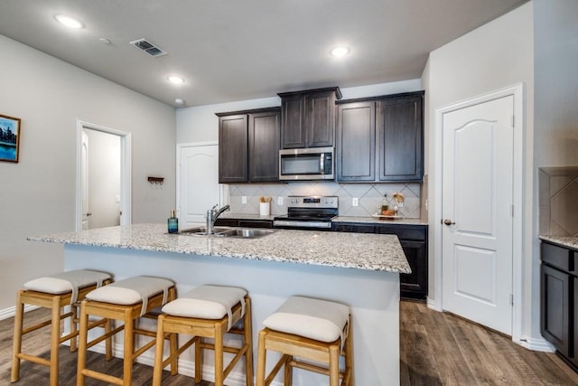 kitchen featuring sink, stainless steel appliances, dark hardwood / wood-style floors, dark brown cabinetry, and a center island with sink