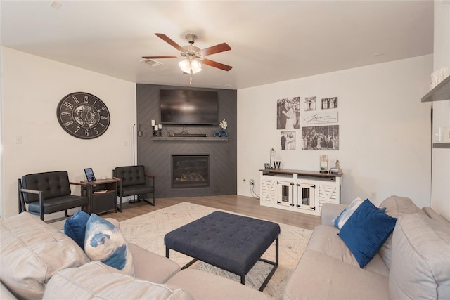 living room featuring a ceiling fan, wood finished floors, visible vents, and a large fireplace