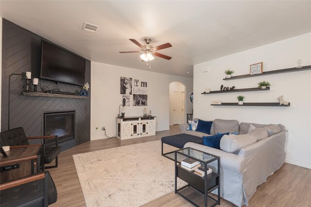 living area featuring a large fireplace, baseboards, wood finished floors, arched walkways, and a ceiling fan