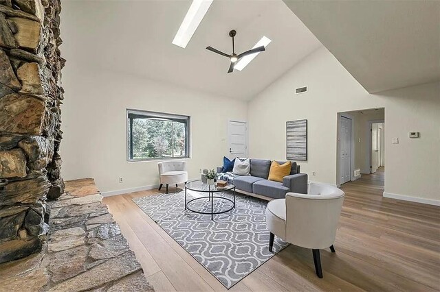 living room featuring hardwood / wood-style flooring, a skylight, high vaulted ceiling, and ceiling fan