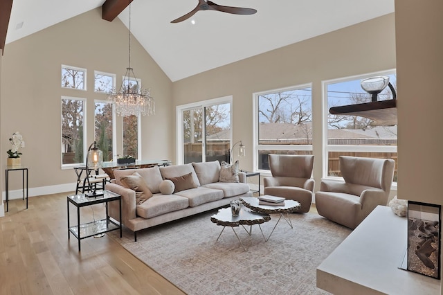 living room featuring high vaulted ceiling, light wood-style flooring, ceiling fan with notable chandelier, baseboards, and beamed ceiling