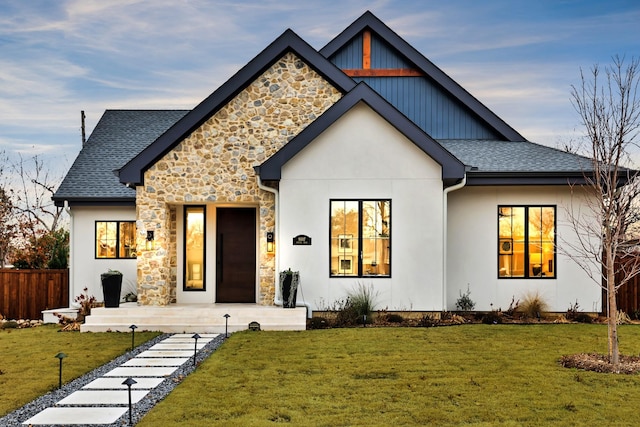 modern farmhouse featuring a front yard, fence, stone siding, and stucco siding