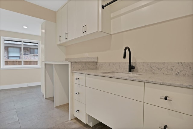 kitchen with white cabinetry, sink, and light stone counters