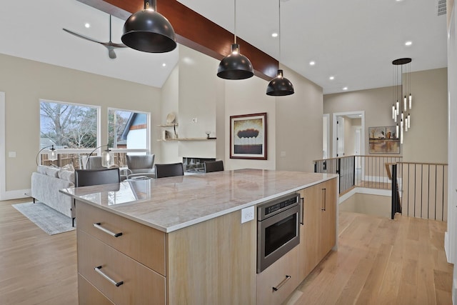 kitchen with pendant lighting, light stone counters, stainless steel microwave, a kitchen island, and light brown cabinetry