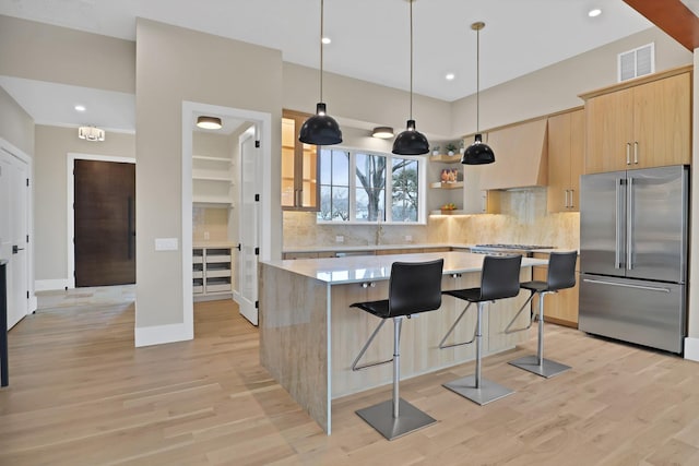 kitchen with a breakfast bar area, a center island, high end fridge, light brown cabinets, and light wood-type flooring