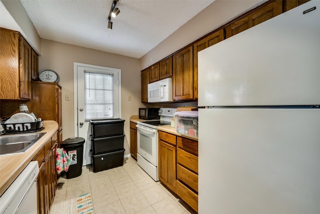 kitchen featuring sink, white appliances, light tile patterned floors, track lighting, and a textured ceiling