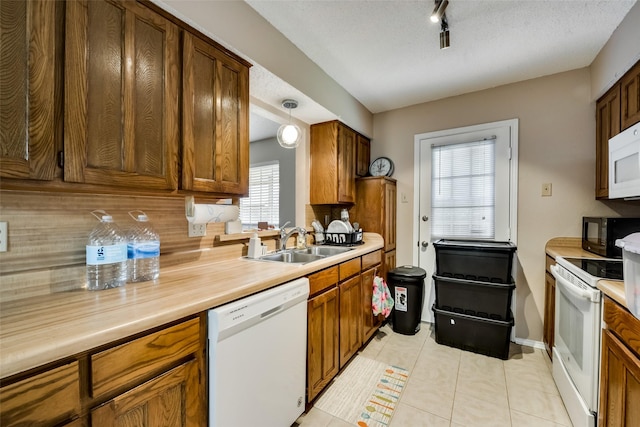 kitchen featuring pendant lighting, sink, white appliances, light tile patterned floors, and a textured ceiling