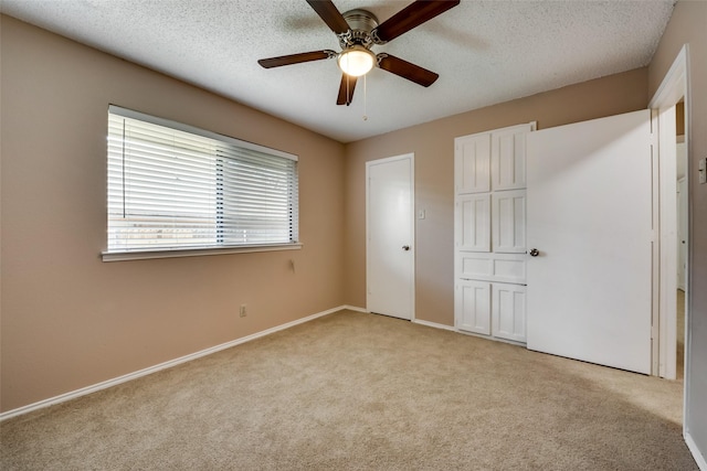 unfurnished bedroom with multiple closets, light colored carpet, a textured ceiling, and ceiling fan