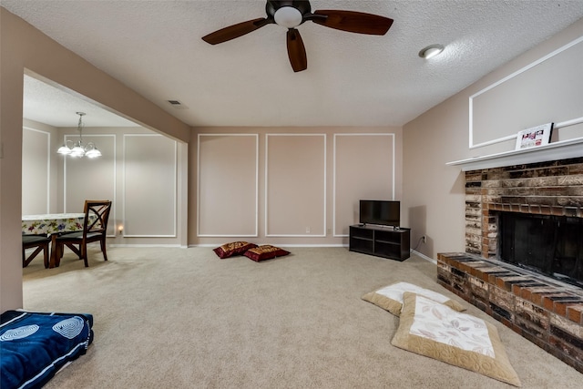 living room with a brick fireplace, ceiling fan with notable chandelier, light colored carpet, and a textured ceiling