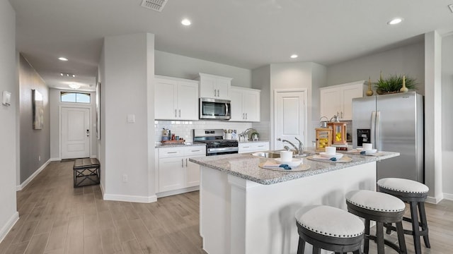 kitchen featuring white cabinetry, appliances with stainless steel finishes, a breakfast bar, and a center island with sink