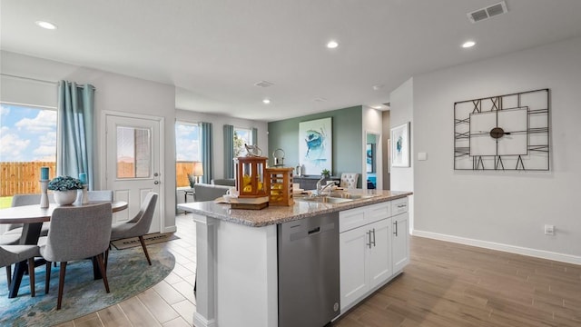 kitchen with sink, dishwasher, white cabinetry, light stone counters, and an island with sink