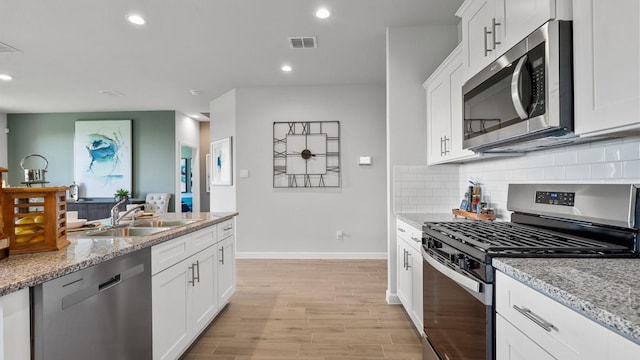 kitchen with white cabinetry, appliances with stainless steel finishes, sink, and light stone counters