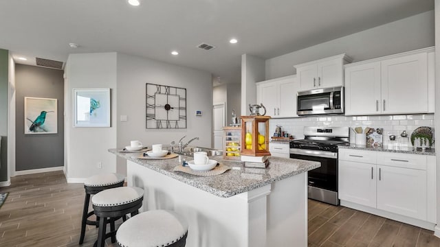 kitchen featuring stainless steel appliances, white cabinetry, sink, and a center island with sink