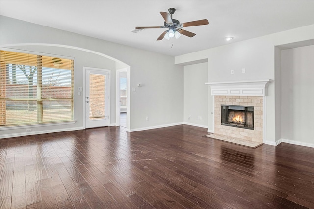 unfurnished living room featuring a tiled fireplace, dark wood-type flooring, and ceiling fan