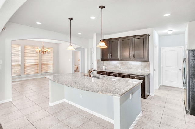 kitchen with a kitchen island with sink, sink, decorative light fixtures, and light stone countertops