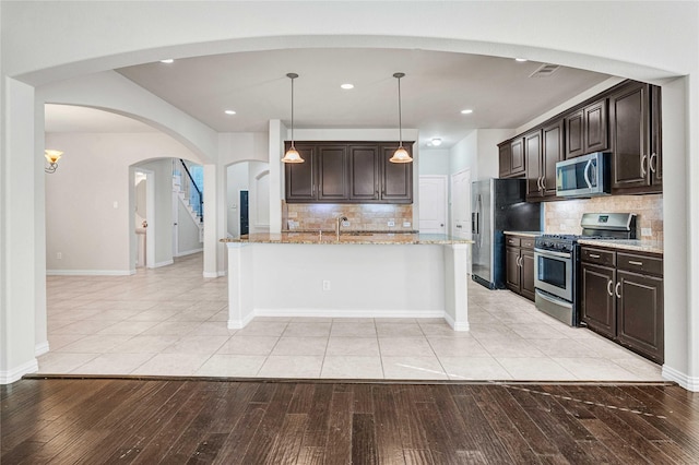 kitchen with light stone counters, appliances with stainless steel finishes, pendant lighting, light hardwood / wood-style floors, and backsplash