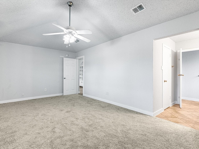 unfurnished room with vaulted ceiling, ceiling fan, light colored carpet, and a textured ceiling