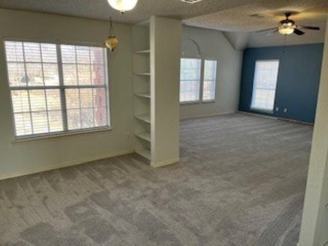 carpeted spare room with ceiling fan, built in shelves, and a textured ceiling