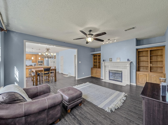 living room with a fireplace, ceiling fan with notable chandelier, dark wood-type flooring, and a textured ceiling