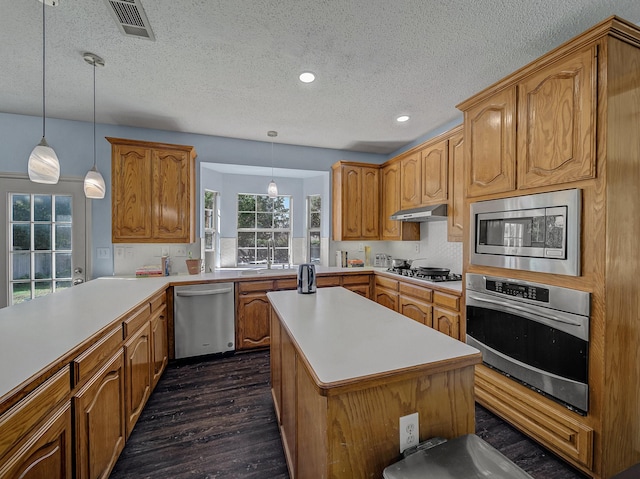 kitchen with appliances with stainless steel finishes, a center island, pendant lighting, and dark hardwood / wood-style floors