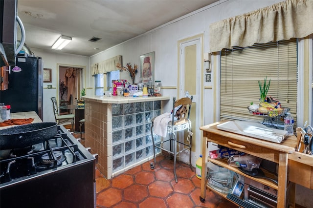 kitchen with black gas range oven, tile countertops, and stainless steel refrigerator