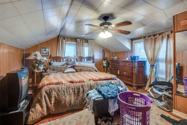 bedroom with vaulted ceiling, wooden walls, and ceiling fan