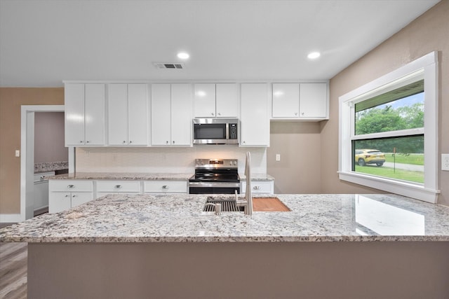 kitchen with stainless steel appliances, white cabinetry, a center island, and light stone counters