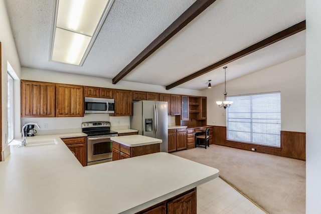 kitchen with sink, appliances with stainless steel finishes, wooden walls, decorative light fixtures, and kitchen peninsula