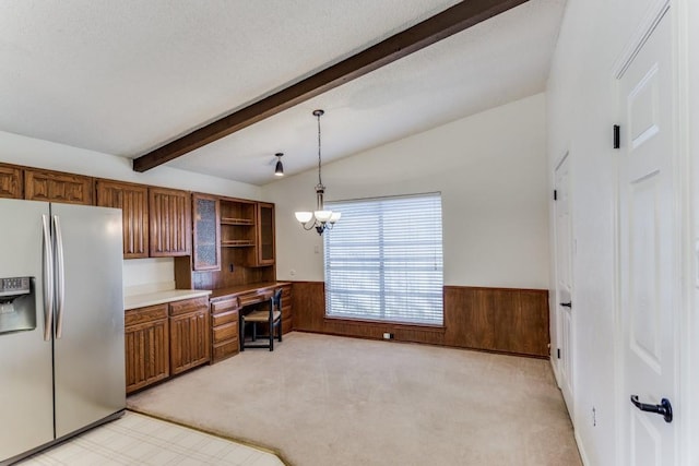 kitchen with built in desk, pendant lighting, wooden walls, light colored carpet, and stainless steel fridge with ice dispenser