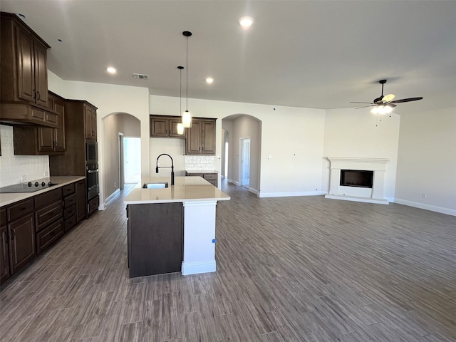 kitchen featuring dark brown cabinetry, black electric stovetop, an island with sink, and backsplash