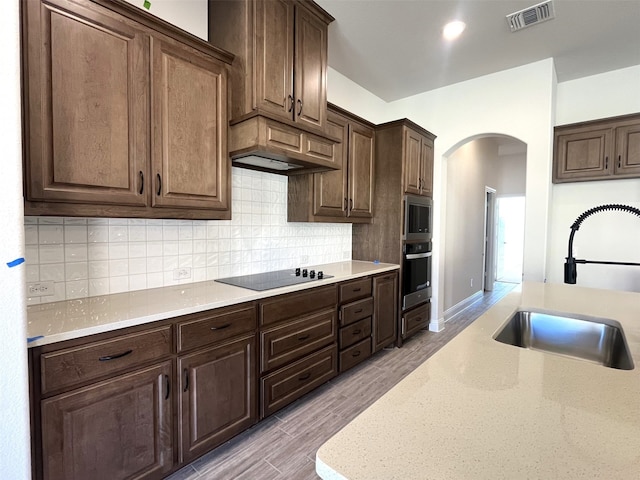 kitchen featuring sink, appliances with stainless steel finishes, dark brown cabinets, light stone counters, and light wood-type flooring