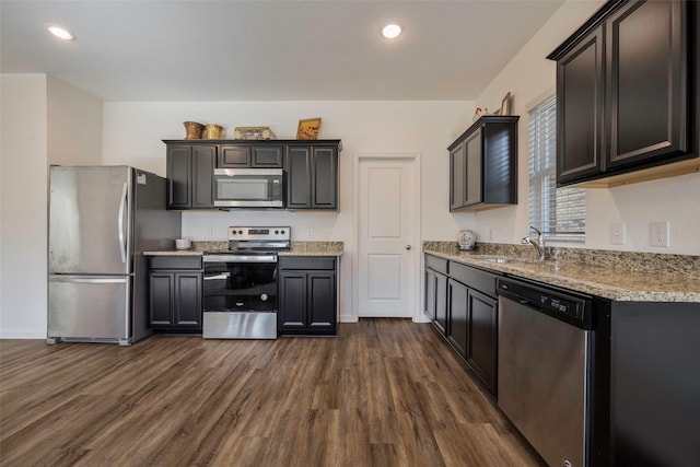 kitchen with light stone countertops, appliances with stainless steel finishes, dark hardwood / wood-style floors, and sink