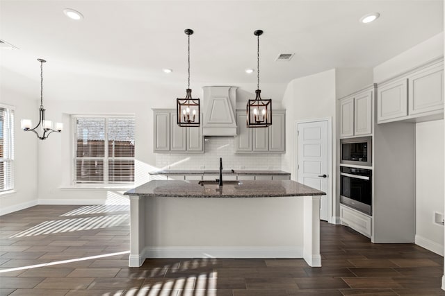 kitchen featuring built in microwave, dark stone counters, a chandelier, and stainless steel oven