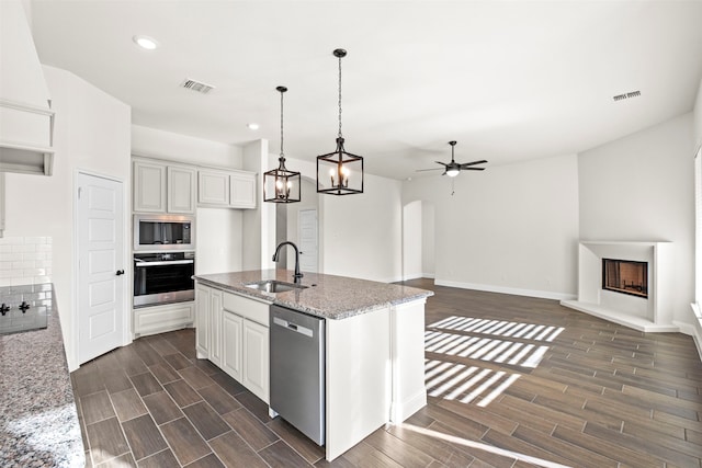 kitchen with sink, white cabinetry, stainless steel appliances, light stone counters, and a center island with sink