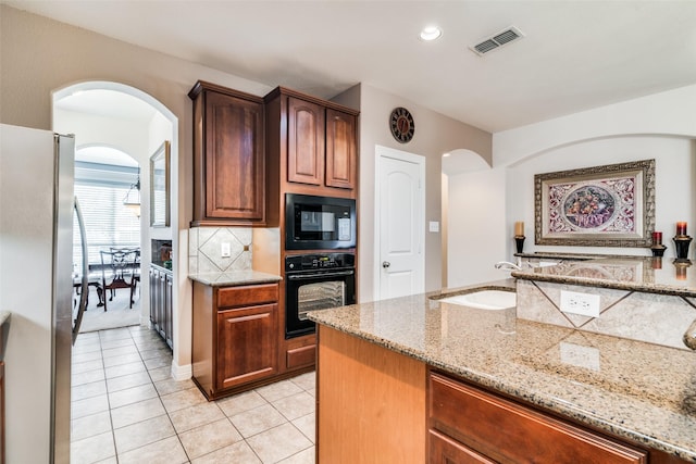 kitchen with light tile patterned flooring, sink, light stone counters, black appliances, and backsplash