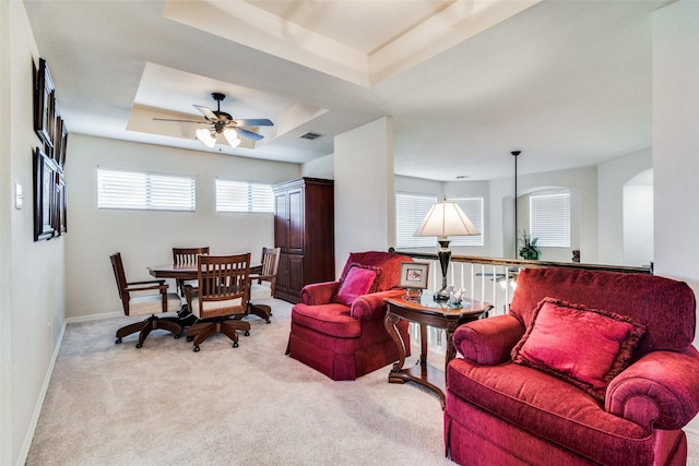 carpeted living room with a raised ceiling, plenty of natural light, and ceiling fan