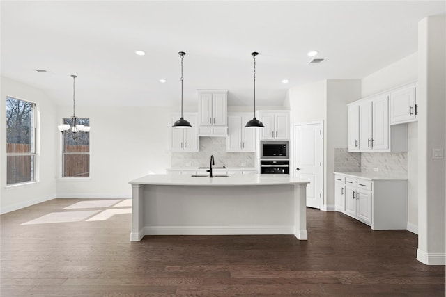 kitchen featuring white cabinets, an island with sink, stainless steel microwave, and oven