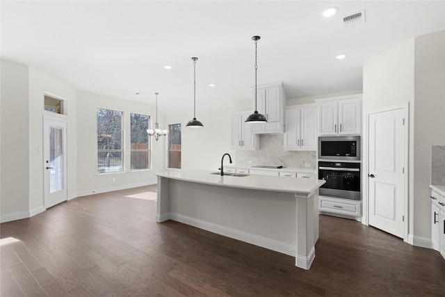 kitchen featuring sink, appliances with stainless steel finishes, backsplash, white cabinets, and a center island with sink