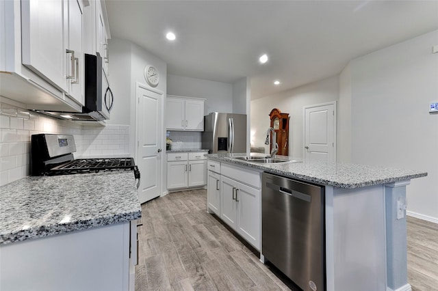 kitchen featuring light wood finished floors, tasteful backsplash, white cabinets, stainless steel appliances, and a sink