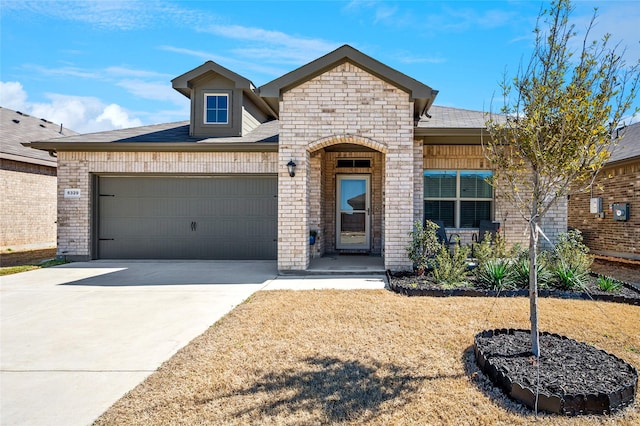 french country inspired facade with driveway, stone siding, roof with shingles, a garage, and brick siding