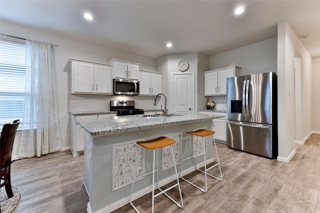 kitchen with a sink, stainless steel appliances, light wood-style floors, white cabinetry, and a kitchen island with sink