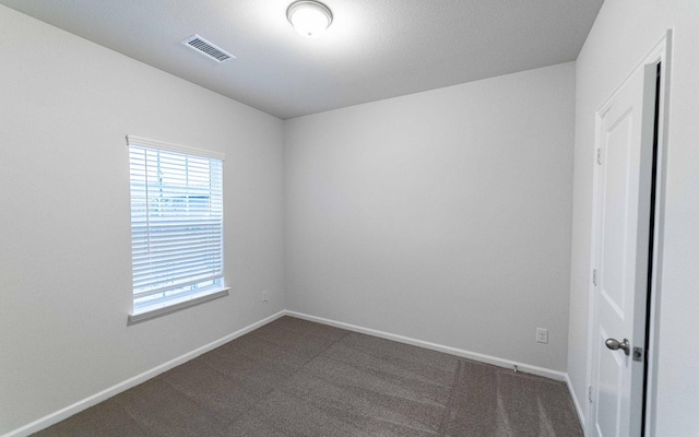 spare room with visible vents, dark carpet, and baseboards