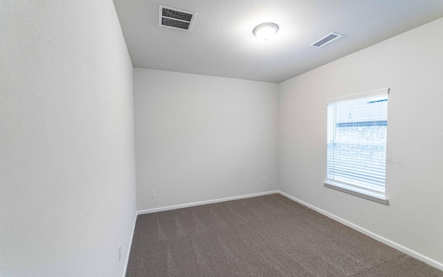 empty room with baseboards, visible vents, and dark carpet