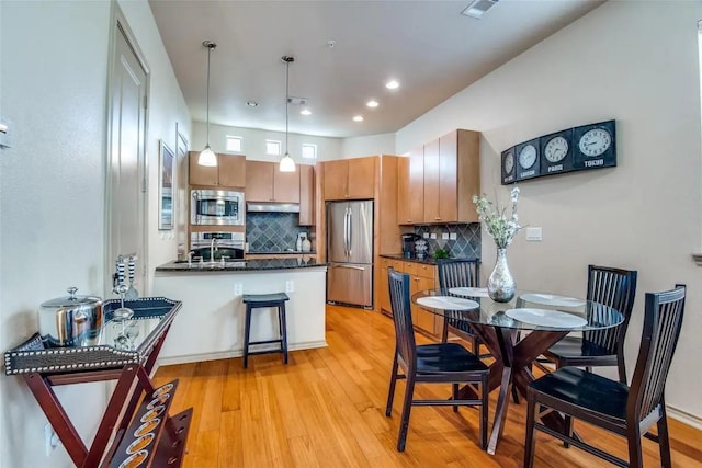 kitchen with light hardwood / wood-style flooring, appliances with stainless steel finishes, backsplash, decorative light fixtures, and kitchen peninsula