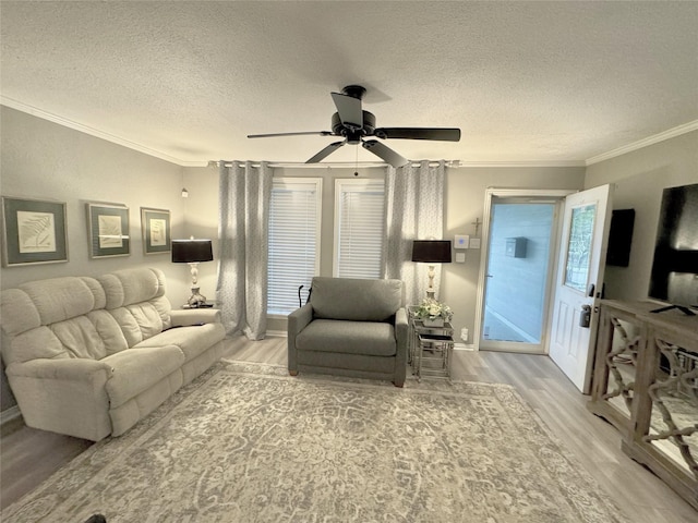 living room featuring ceiling fan, ornamental molding, a textured ceiling, and light wood-type flooring